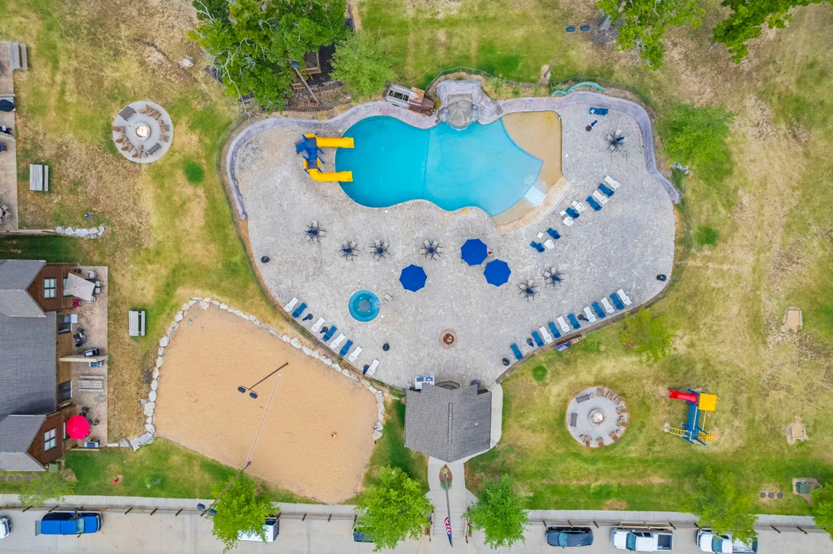 A lively pool area featuring a water slide, sand volleyball court, lounge chairs, and a fire pit, with guests swimming, playing, and relaxing. The space is designed for both active play and group gatherings, echoing the summer highlights and shared moments described in the section.