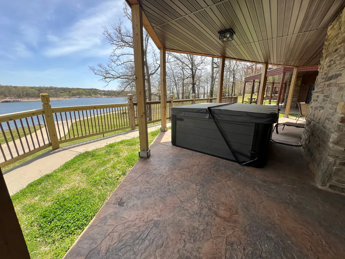 A serene hot tub sits on a private deck overlooking Table Rock Lake, framed by a wooden railing. The tranquil water of the lake stretches beyond, complemented by the cozy outdoor setup of the hot tub. The mood is peaceful, inviting guests to unwind while soaking up breathtaking lake views, regardless of the season.