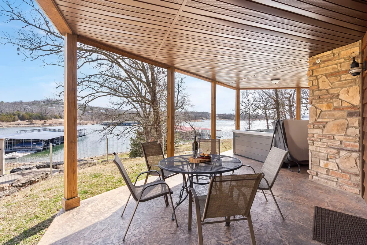 An exterior shot highlighting an outdoor dining table overlooking the lake, a hot tub, and lush surrounding trees. The serene scene invites guests to dine al fresco, relax in the hot tub, and take in the tranquil water views, embodying the blend of social spaces and peaceful retreats.