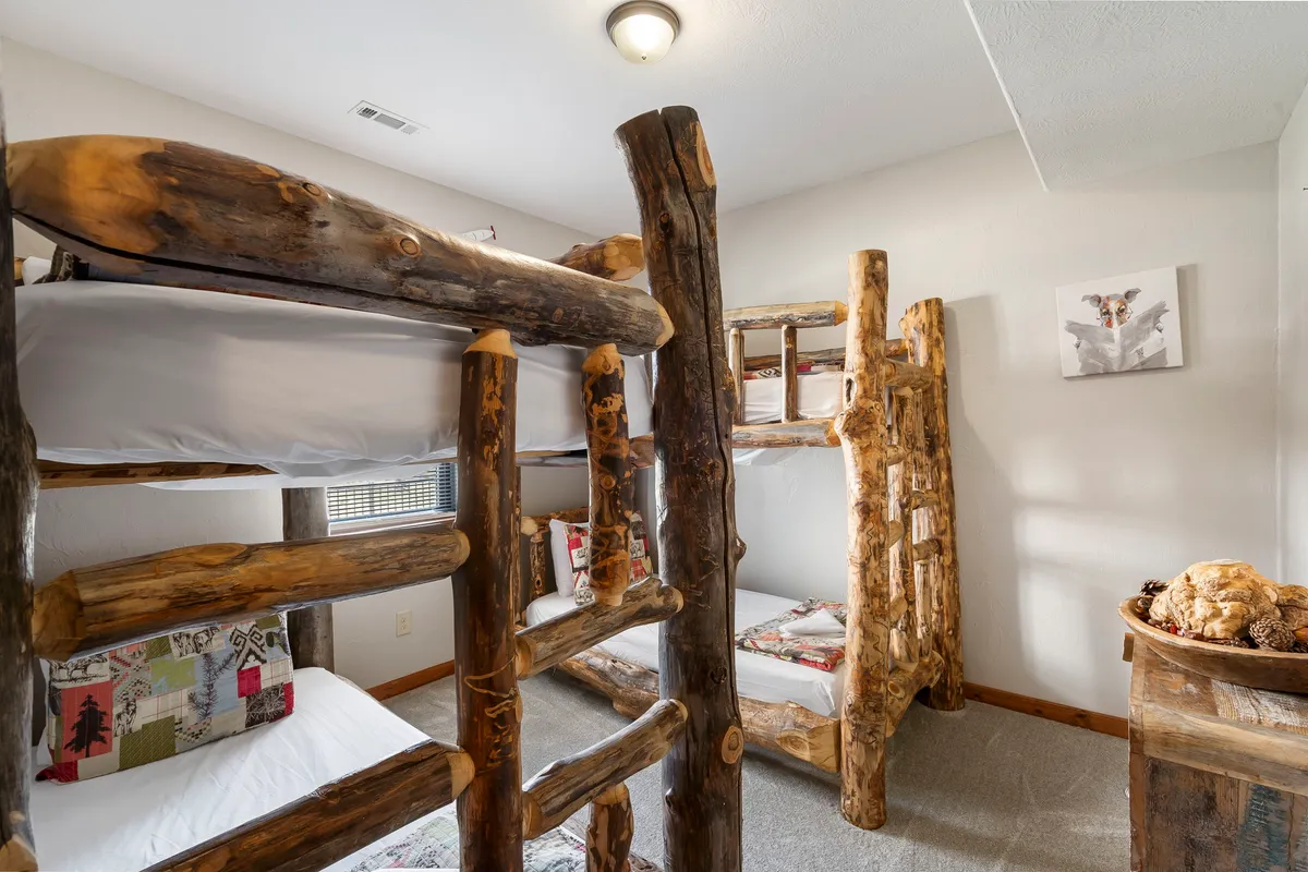 A cozy bunk room with wooden accents and bunk beds adorned with decorative pillows. The space radiates warmth and playfulness, perfect for kids or teens to enjoy late-night conversations or mornings filled with laughter.