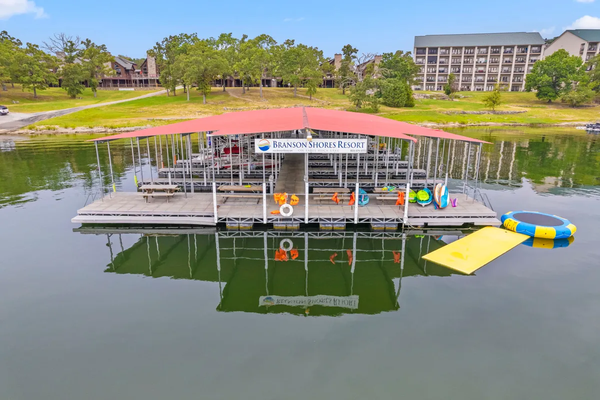 This vibrant image captures a lively lakeside dock with a floating playground, colorful kayaks, and clear resort signage. Guests enjoy activities such as boating, fishing, and swimming, all set against a sparkling lake backdrop. The dock area invites family gatherings and showcases a wide range of water-based fun.