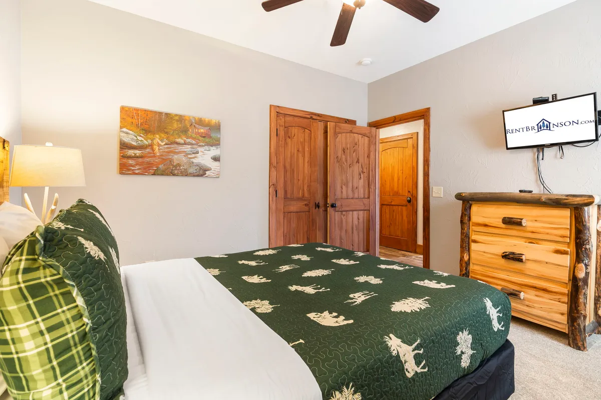 A comfortable queen bedroom featuring a green patterned bedspread, wooden furniture, and artwork on the wall. The room invites relaxation and is perfectly suited for restful nights on the main level.